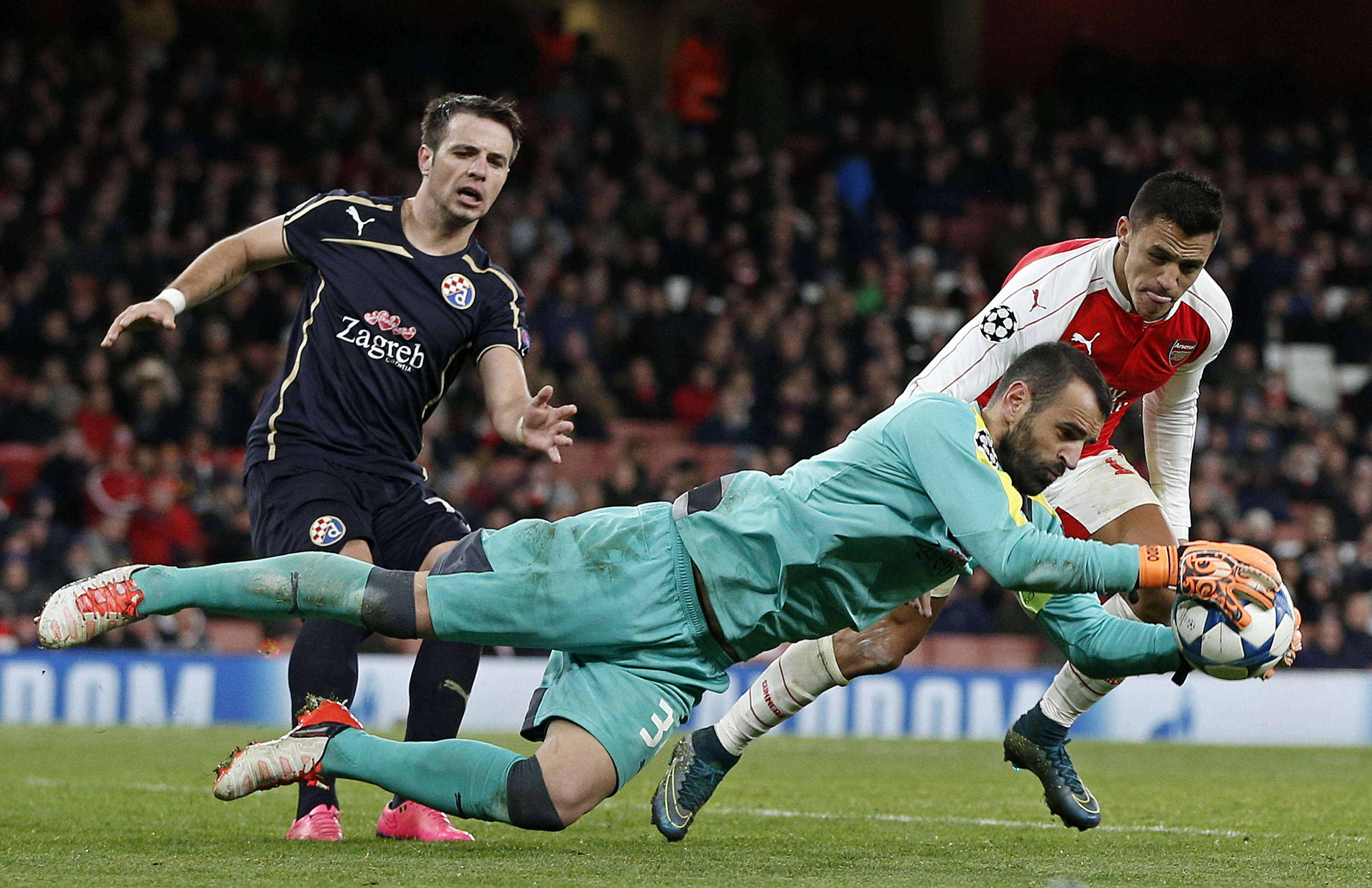Dinamo Zagreb's goalkeeper from Portugal Eduardo (Foreground) defends the ball from Arsenal's Chilean striker Alexis Sanchez (Back R) during their UEFA Champions League Group F football match between Arsenal and GNK Dinamo Zagreb at The Emirates Stadium in London on November 24, 2015. AFP PHOTO / ADRIAN DENNIS / AFP / ADRIAN DENNIS (Photo credit should read ADRIAN DENNIS/AFP/Getty Images)